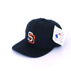 May include: Navy blue baseball cap featuring the San Diego Padres logo in white and orange. The cap has a curved brim and a tag with a Major League Baseball logo.