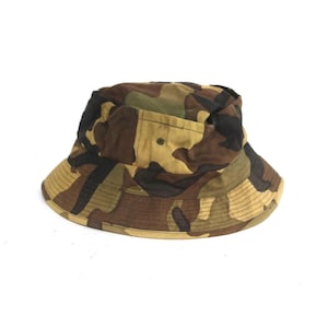 Può includere: Un cappello a secchiello mimetico con un motivo marrone, verde e beige.