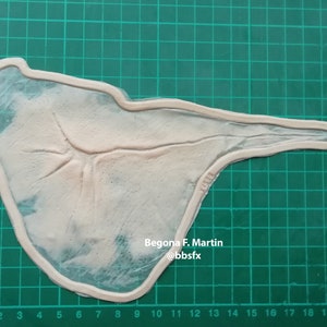 Peut inclure: Gros plan d'un moule en silicone blanc sur un tapis de coupe vert. Le moule est en forme de main humaine avec un motif de veines détaillé. Le texte "Begona F. Martin @bbsfx" est imprimé sur le moule.