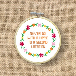 Puede incluir: Aro de bordado blanco con un borde floral y el texto "NEVER GO WITH A HIPPIE TO A SECOND LOCATION" en naranja.