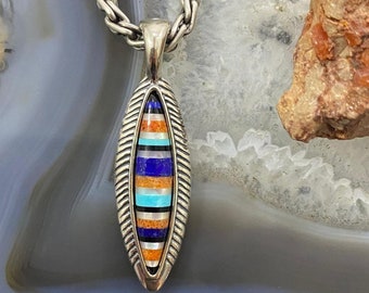 May include: Silver pendant necklace with an elongated, leaf-shaped pendant. The pendant features a colorful inlay of orange, blue, turquoise, and black stones. The necklace chain is a thick, braided design.
