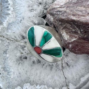 May include: A silver ring featuring a fan-shaped inlay design. The inlay consists of alternating segments of green malachite and white stone, arranged in a radial pattern around a small, central, oval-shaped red stone at the base of the fan.