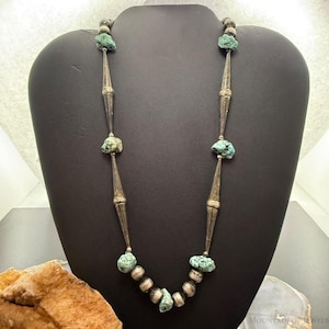 May include: A necklace featuring raw, light blue-green turquoise nuggets interspersed with elongated, tapered silver beads and smaller round silver beads. The design alternates between the rough turquoise stones and the smooth, metallic silver components.