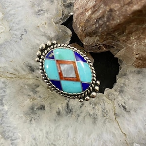 May include: A silver ring featuring a blue, turquoise, and red inlay design. The inlay is in a diamond shape and is surrounded by a silver rope border.