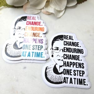 May include: Two stickers featuring a black and white portrait of a woman with glasses. The stickers have the text "REAL CHANGE, ENDURING CHANGE, HAPPENS ONE STEP AT A TIME" in various colors.