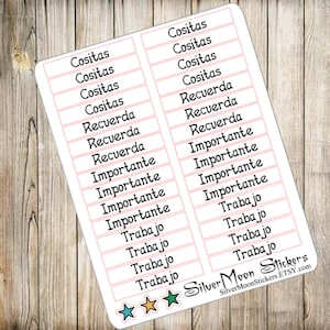 May include: A sheet of stickers with various Spanish words in a black font, including "Cositas," "Recuerda," "Importante," and "Trabajo." Each word is in a pink-lined box. The sticker sheet has a white background and a wooden surface.