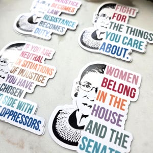 May include: Set of four colorful stickers featuring a portrait of Ruth Bader Ginsburg with inspirational quotes. The quotes include "When injustice becomes law, resistance becomes duty", "Fight for the things you care about", "If you are neutral in situations of injustice you have chosen to side with oppressors", and "Women belong in the house and the senate".