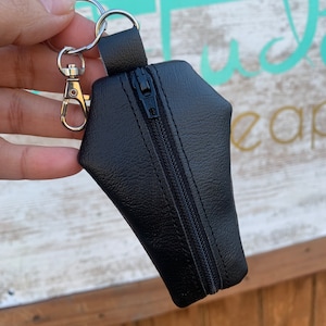 Pode incluir: Bolsa preta de couro sint&eacute;tico com z&iacute;per em forma de caix&atilde;o com um chaveiro prateado.
