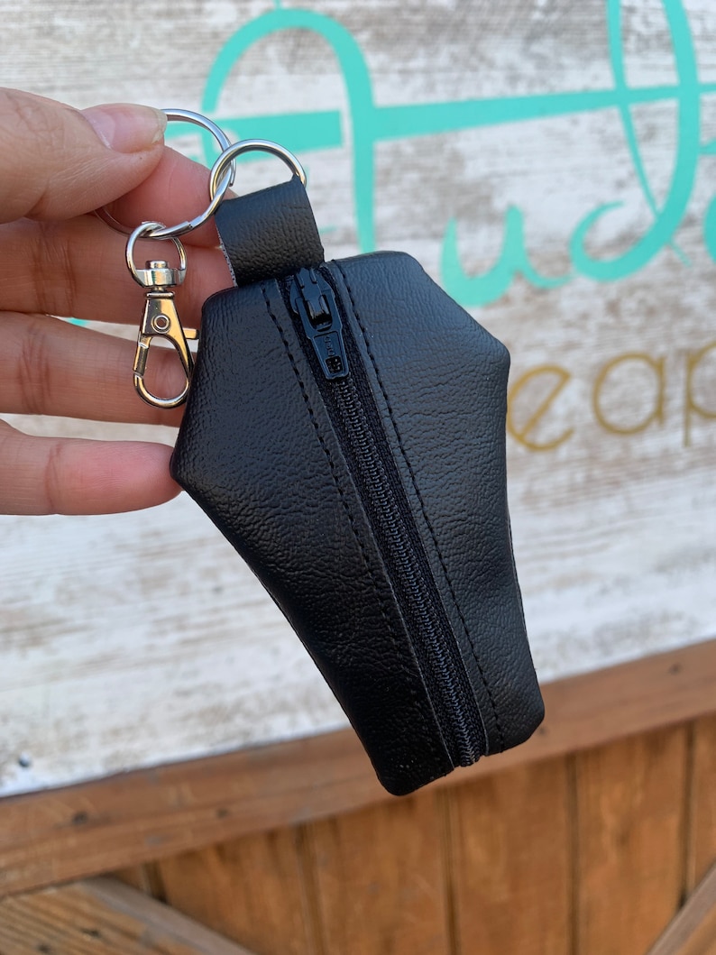 Pode incluir: Bolsa preta de couro sint&eacute;tico com z&iacute;per em forma de caix&atilde;o com um chaveiro prateado.