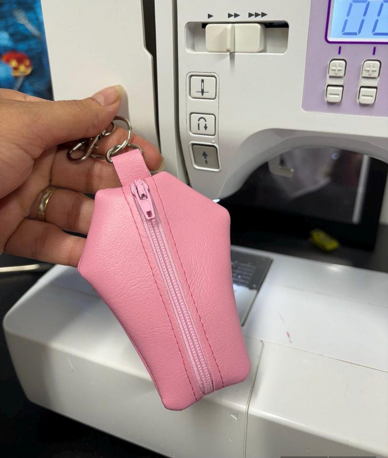 Pode incluir: Uma bolsa rosa com z&iacute;per em forma de caix&atilde;o. A bolsa est&aacute; pendurada em um chaveiro prateado.
