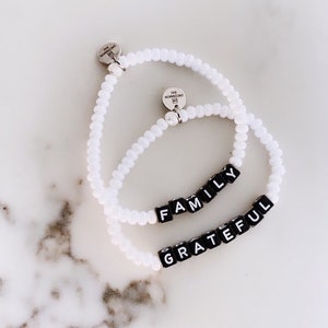May include: Two white beaded bracelets with black letter beads spelling out "FAMILY" and "GRATEFUL".