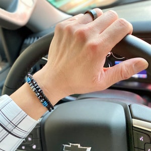 May include: A black beaded bracelet with the words "FOR REALLY" spelled out in silver beads. The bracelet is worn on a person's wrist.