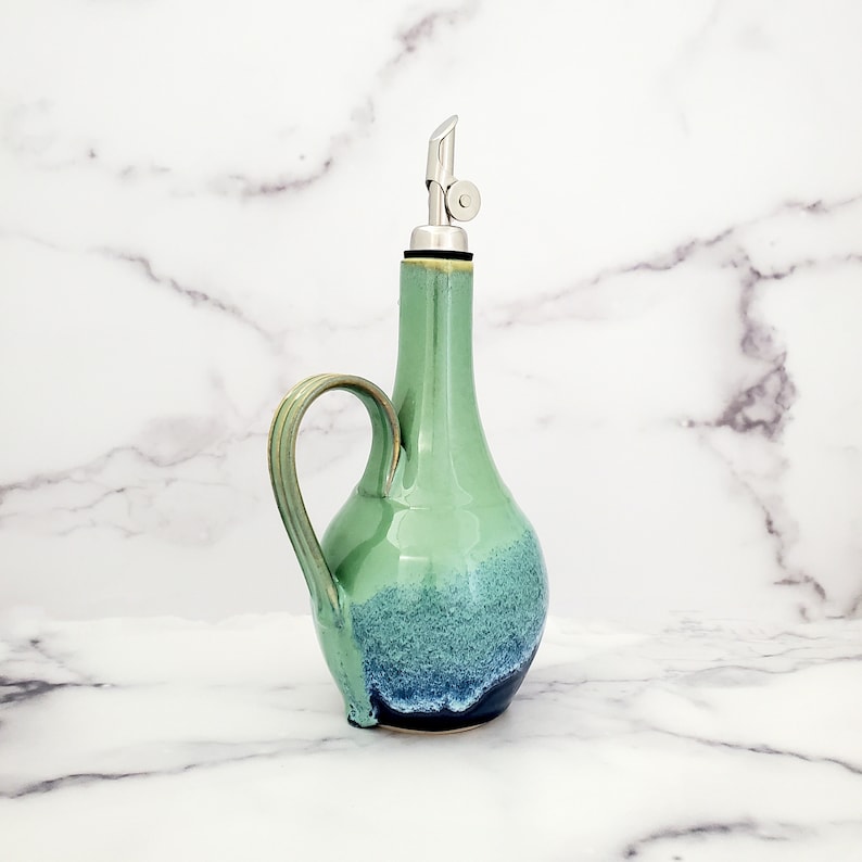 May include: A green and blue ceramic oil and vinegar bottle with a stainless steel pour spout and a handle.