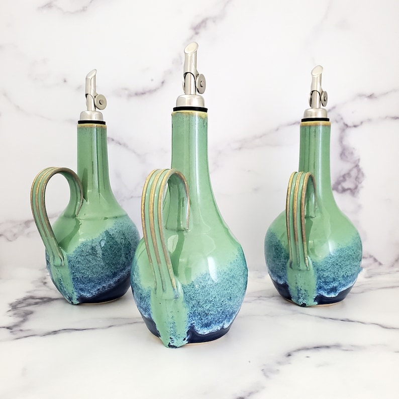 May include: Three ceramic oil and vinegar bottles with green and blue glaze. Each bottle has a silver pour spout and a handle.
