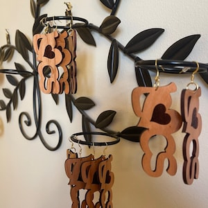 May include: Three pairs of wooden earrings with the word "Love" carved into them. The earrings are hanging from a black metal branch with leaves.