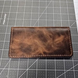 May include: A brown leather wallet with a distressed finish and stitching around the edges.