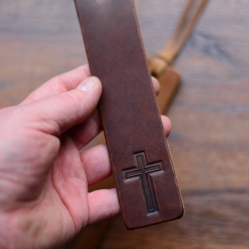 May include: A brown leather bookmark with a cross embossed on it.