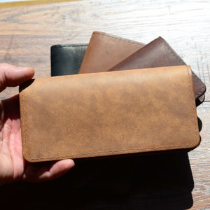 May include: A brown leather wallet with a stitched edge. The wallet is folded in half and has a worn, distressed look.