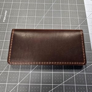 May include: A brown leather wallet with a stitched edge.