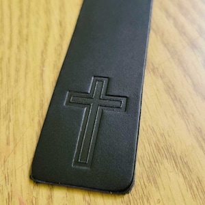 May include: Black leather bookmark with a cross embossed on the front.
