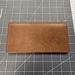May include: A brown leather wallet with a stitched edge.