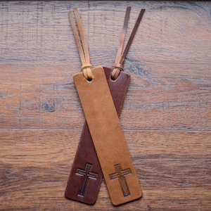 May include: Two leather bookmarks with cross designs. One bookmark is brown and the other is tan.