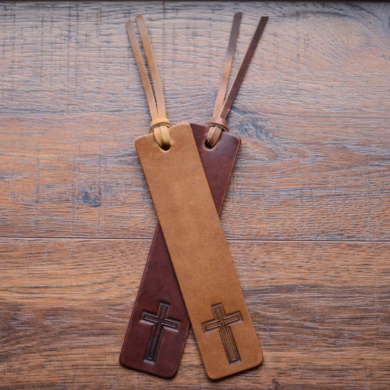 May include: Two leather bookmarks with cross designs. One bookmark is brown and the other is tan.