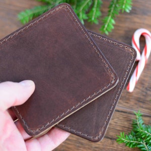 May include: Two brown leather coasters with stitched edges. The coasters are stacked on top of each other.