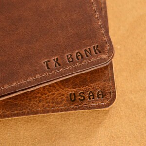 May include: Close-up of two brown leather wallets with the names "TX BANK" and "USAA" embossed on them.