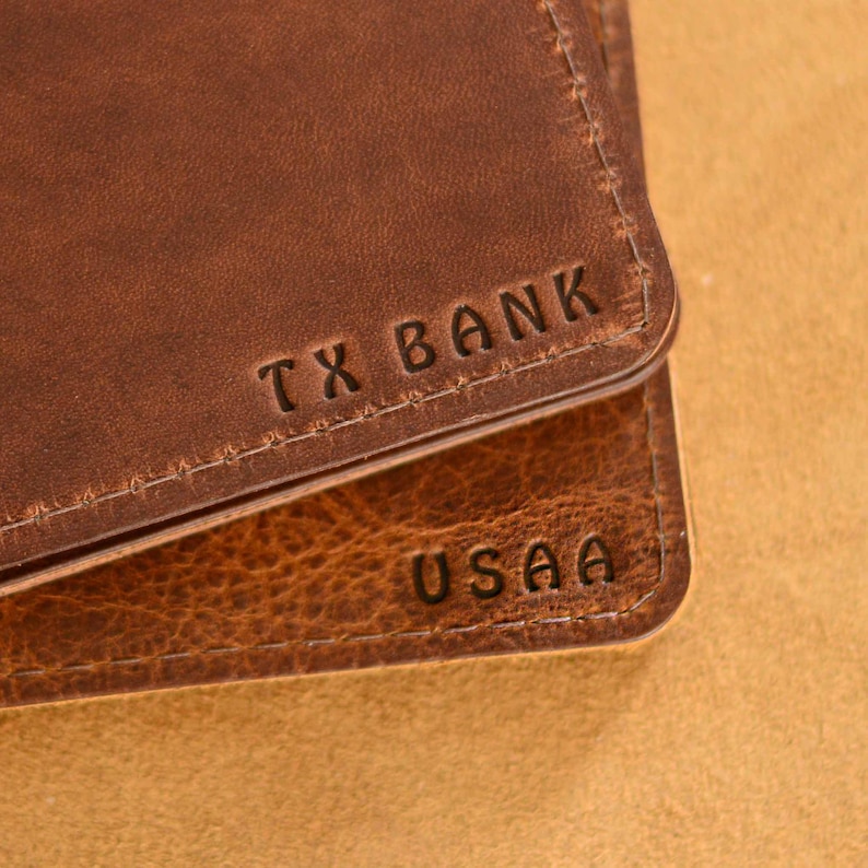 May include: Close-up of two brown leather wallets with the names "TX BANK" and "USAA" embossed on them.