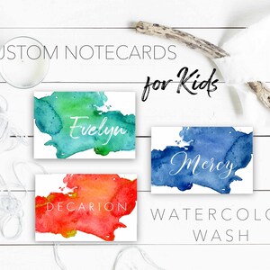 Puede incluir: Tres tarjetas de notas de acuarela con nombres personalizados, "Evelyn", "Mercy" y "Decarion", en escritura blanca. Las tarjetas de notas tienen un fondo de lavado de acuarela en tonos de azul, verde y naranja. El texto "CUSTOM NOTECARDS for Kids WATERCOLOR WASH" está impreso debajo de las tarjetas de notas.