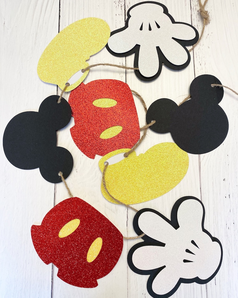Puede incluir: Una guirnalda con recortes de fieltro rojo, amarillo y negro de la cabeza, las manos y los zapatos de Mickey Mouse. Los recortes est&aacute;n decorados con purpurina.