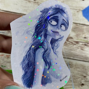 Könnte beinhalten: Ein holografischer Aufkleber mit einer blauen und weißen Illustration einer Frau mit langen Haaren, die eine Krone und einen Schleier trägt. Der Hintergrund ist weiß mit schimmernden, regenbogenfarbenen Sternen.