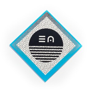 Könnte beinhalten: Ein geometrisches Design in Schwarzweiß mit einem Kreis, der die Buchstaben "EA" in weißer Schrift enthält. Das Design befindet sich auf einem blauen und silbernen rautenförmigen Hintergrund.