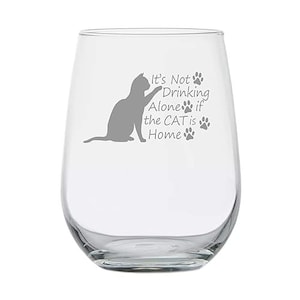 May include: A clear stemless wine glass with a gray cat silhouette and the text "It's Not Drinking Alone if the CAT is Home" with paw prints. The glass is designed for wine and other beverages.