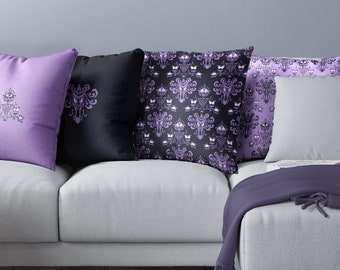 May include: A light gray couch with four throw pillows. The pillows have a black and purple pattern with a ghostly figure and a repeating pattern of butterflies. A purple throw blanket is draped over the arm of the couch.