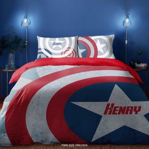 Può includere: Un set di biancheria da letto per letto singolo con un design a scudo di Captain America rosso, bianco e blu. Il piumino e le federe hanno un aspetto usurato e il nome "Henry" è stampato sul piumino.