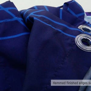 May include: Close-up of a navy blue fabric with a white and blue geometric pattern. The fabric has a hemmed edge and grommets for hanging. "Hemmed finished edges sample" is written in white text at the bottom of the image.