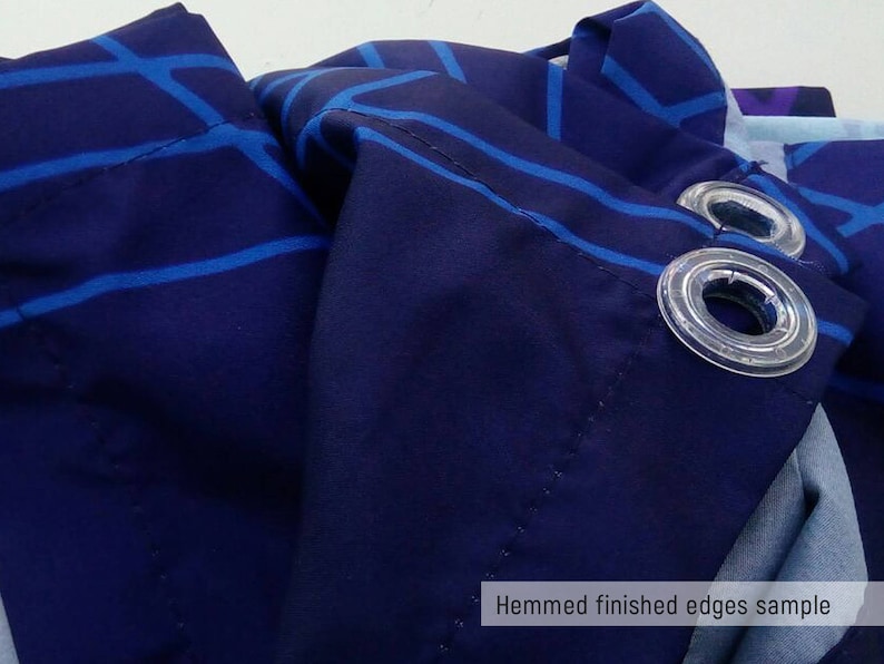 May include: Close-up of a navy blue fabric with a white and blue geometric pattern. The fabric has a hemmed edge and grommets for hanging. "Hemmed finished edges sample" is written in white text at the bottom of the image.