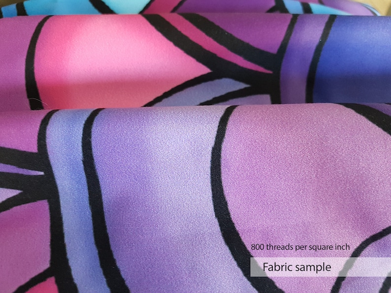 May include: Close-up of a purple, pink, and blue fabric with a geometric pattern. The fabric is smooth and has a subtle sheen. The text "800 threads per square inch" and "Fabric sample" is printed on the fabric.