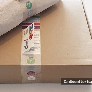 May include: A brown cardboard box with a white fabric item inside. The box has labels with the words "Cool", "Zipped", and "Discover Then". The box is labeled "Cardboard box (sample)".