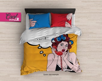 May include: A queen-sized bedding set with a pop art design featuring a woman with red hair and blue rollers in her hair. The woman is on the phone and has a surprised expression. The bedding set has a yellow background with a speech bubble that says "Oh my!" The pillowcases have a blue and red design with a hand reaching out from the fabric.