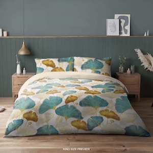 Puede incluir: Juego de cama tamaño King con un patrón repetido de hojas de ginkgo verde azulado y doradas sobre un fondo blanco. El juego incluye una funda nórdica y dos fundas de almohada. El texto "KING SIZE PREVIEW" es visible en la parte inferior de la imagen.
