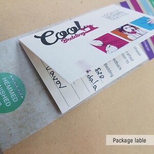 May include: A white package label with the text "Cool Bedding" in black cursive lettering. The label also includes the text "Hemmed Finished Edges" in green on a white circle. The label has a price tag with the text "&pound;20 dala" in black.