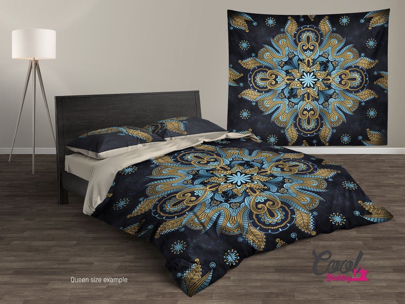 May include: A queen-sized bedding set with a dark blue background and a large, intricate mandala pattern in gold and blue. The mandala features paisley-like designs and floral elements. The bedding set includes a duvet cover, two pillowcases, and a matching throw pillow.