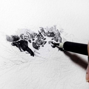 May include: A close-up of a hand holding a black pen, drawing on a white paper. The pen is being used to create a dark, textured area on the paper.