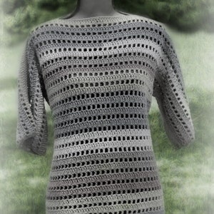 Puede incluir: Un top de crochet gris con un corte holgado y mangas cortas. El top está hecho con un patrón a rayas de diferentes tonos de gris.