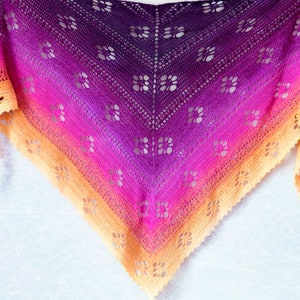 May include: A hand-crocheted shawl in a gradient of colours, shifting from deep purple to vibrant pink and then to a warm orange. The shawl has an open floral pattern, ideal for adding a touch of elegance.