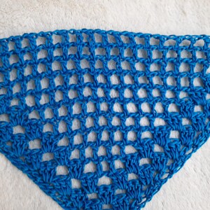 Könnte beinhalten: Ein dreieckiger, blau gehäkelter Schal mit offenem Gewebe. Der Schal ist aus leuchtend blauem Garn gefertigt und weist ein sich wiederholendes Muster aus offenen Quadraten auf. Die Textur ist sichtbar, und der Schal wirkt weich und leicht.