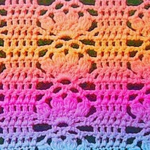 May include: A close-up of a colourful crochet fabric with a repeating pattern of flowers. The fabric is made with a gradient of colours, starting with blue and transitioning to pink, orange, and yellow.
